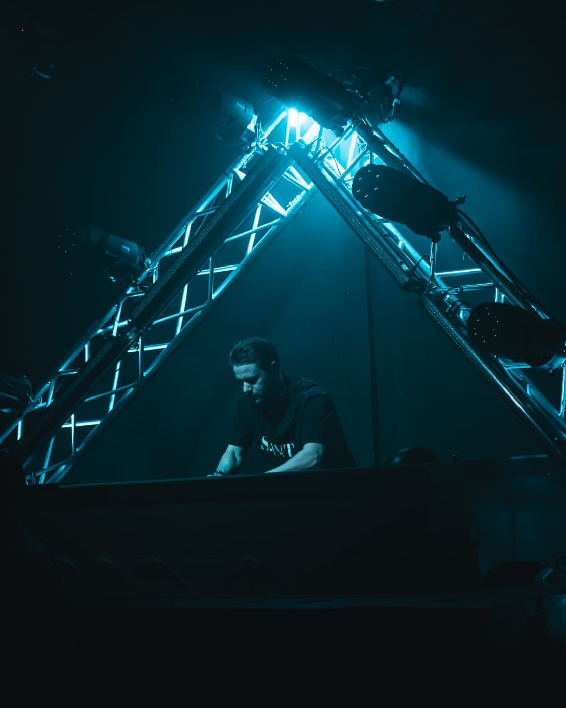 DJ am Pult unter dem türkis beleuchteten Traversendreieck