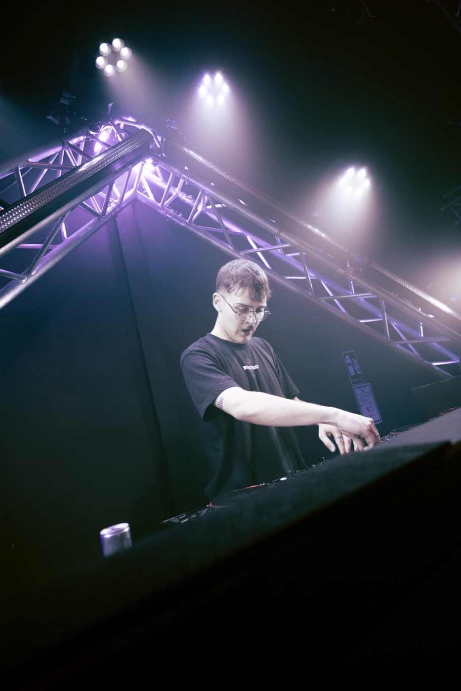 DJ am Mischpult unter violettem Bühnenlicht, Blick durch das Traversenrigg
